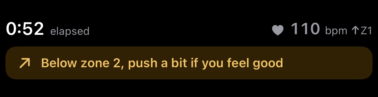 Parameter's execution screen during an interval, showing 0:52 elapsed on the left, a heart rate of 110 bpm with an up arrow and Z1 on the right, and below them an amber banner reading Below zone 2, push a bit if you feel good.